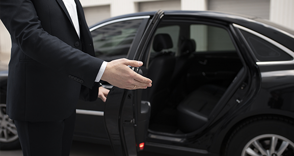 A man and a woman are standing next to a car . the man is holding a suitcase.
