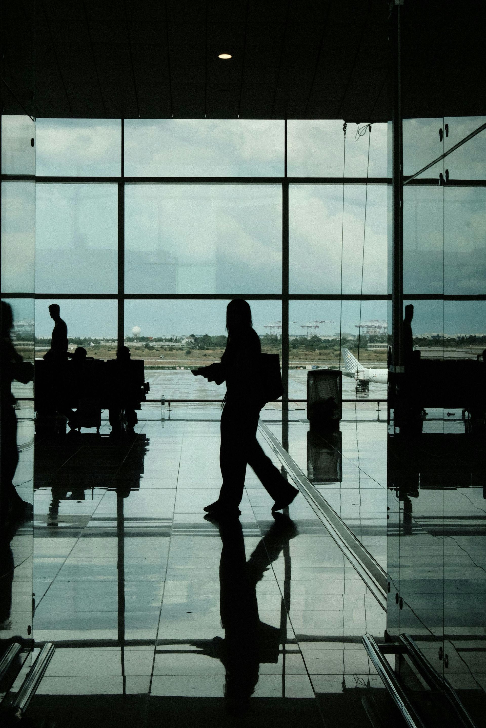 Silhouetted traveler walking through airport terminal with large windows and reflective floor