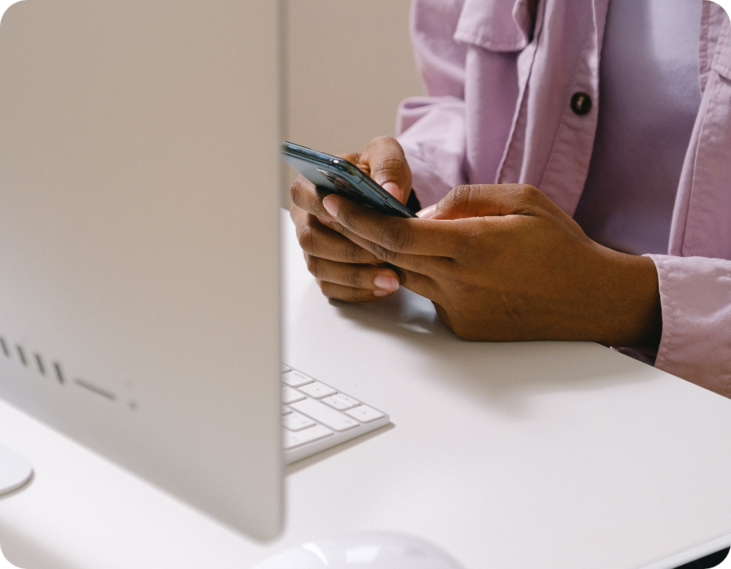 woman holding her phone at her desk in front of her Mac computer