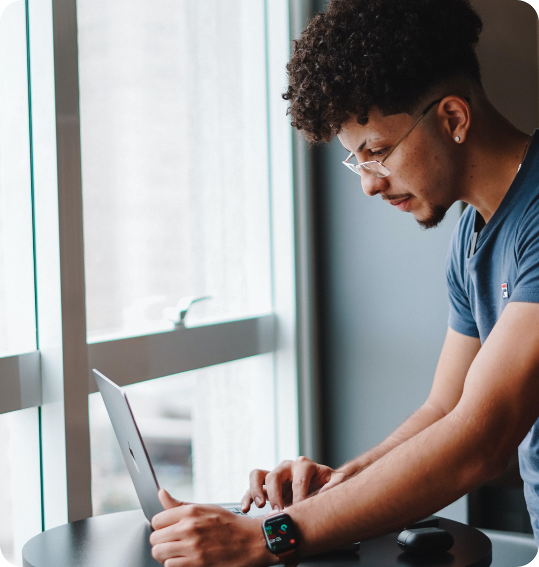 man with glasses looking at his laptop in front of windows