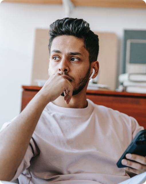man with AirPods in his ears and his phone in his hand looking contemplative