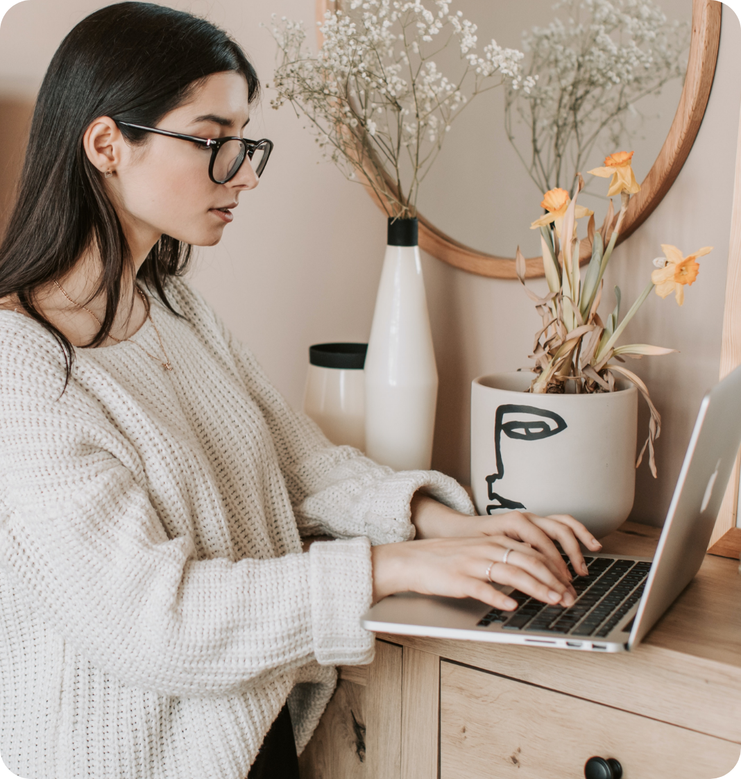 woman with glasses looking and typing on her laptop