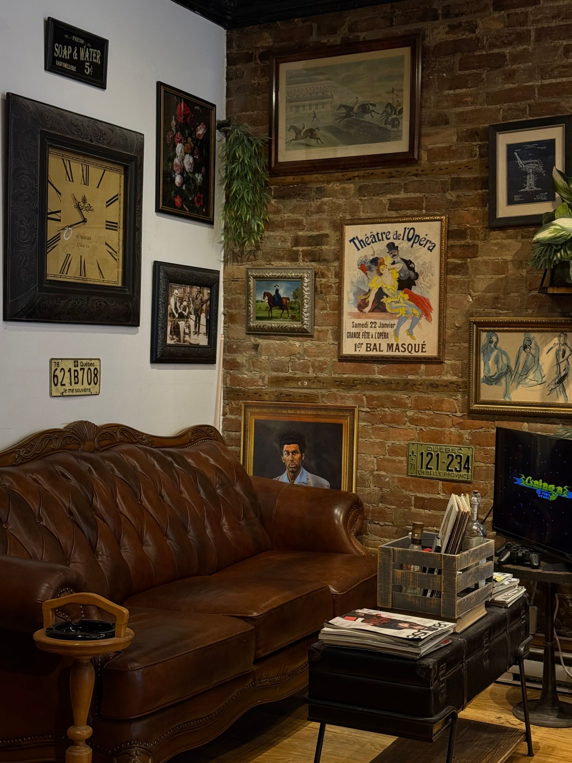 Cozy living room with brown leather sofa, brick wall, and eclectic framed artwork.