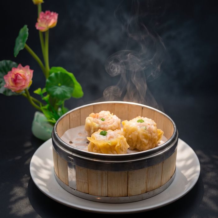 Steaming dumplings in a bamboo basket on a white plate, with pink flowers in the background.