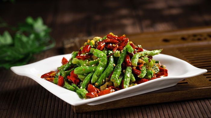 Green beans stir-fried with red chilies on a white plate, served on a dark wooden table