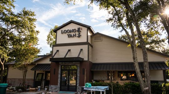 Exterior of Logon Tavern restaurant with tan siding, black awnings, and trees around the entrance