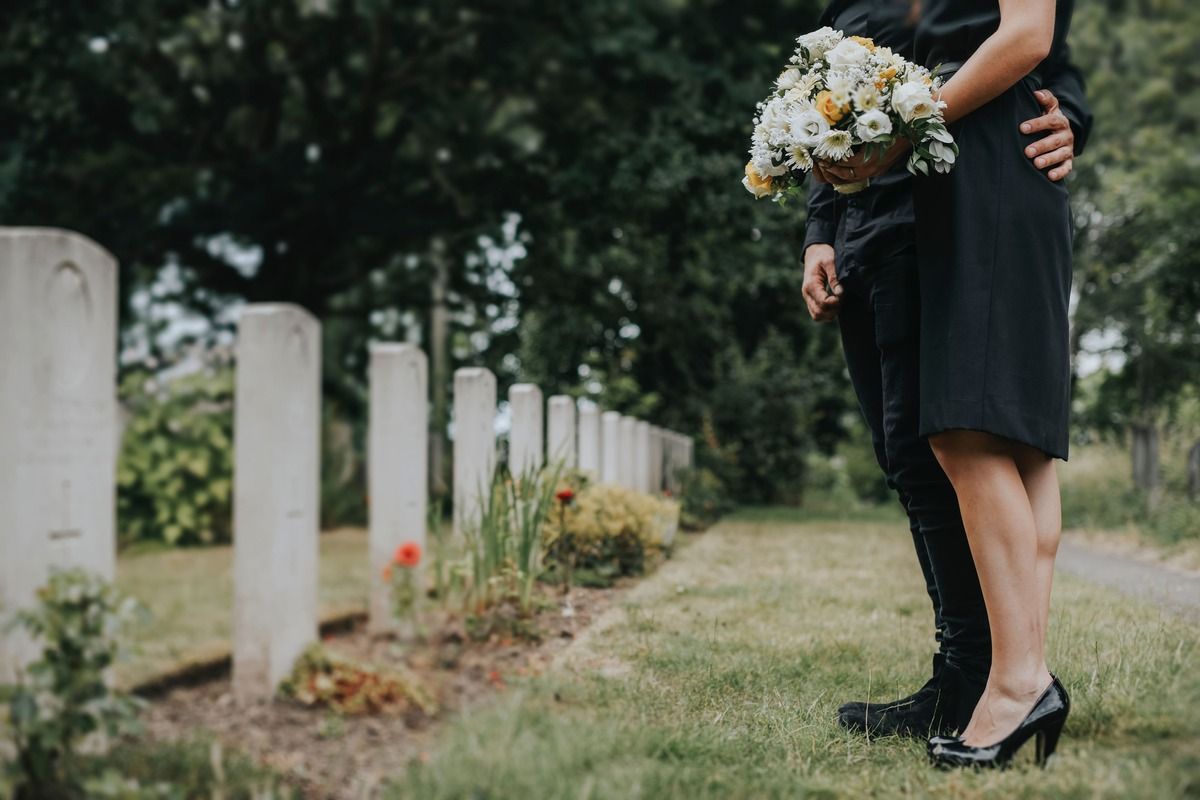 Person in black dress holding bouquet beside cemetery gravestones outdoors