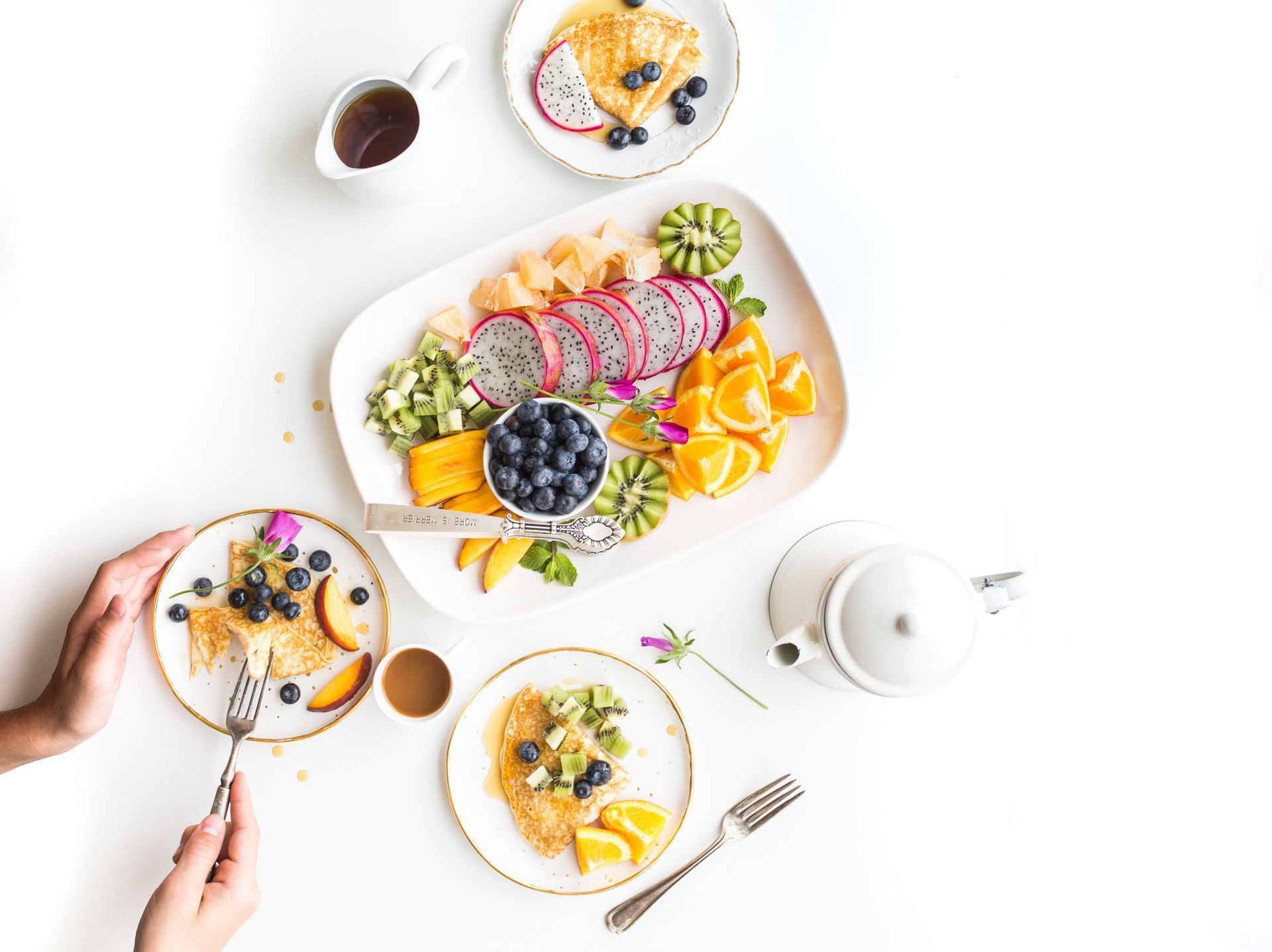 Ontbijt met fruitschaal, pannenkoeken en handen die bestek gebruiken.