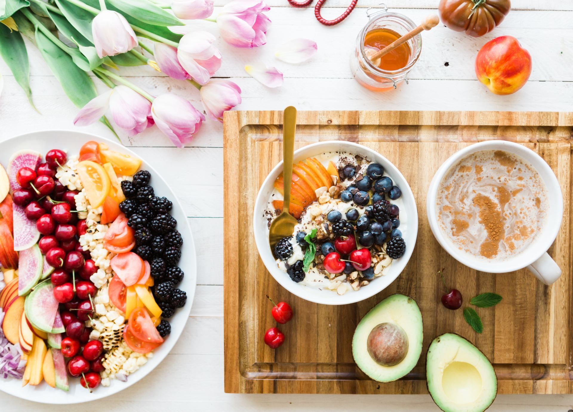 Ontbijt: fruitschaal, havermoutkom met bessen, koffie, honing en avocado.