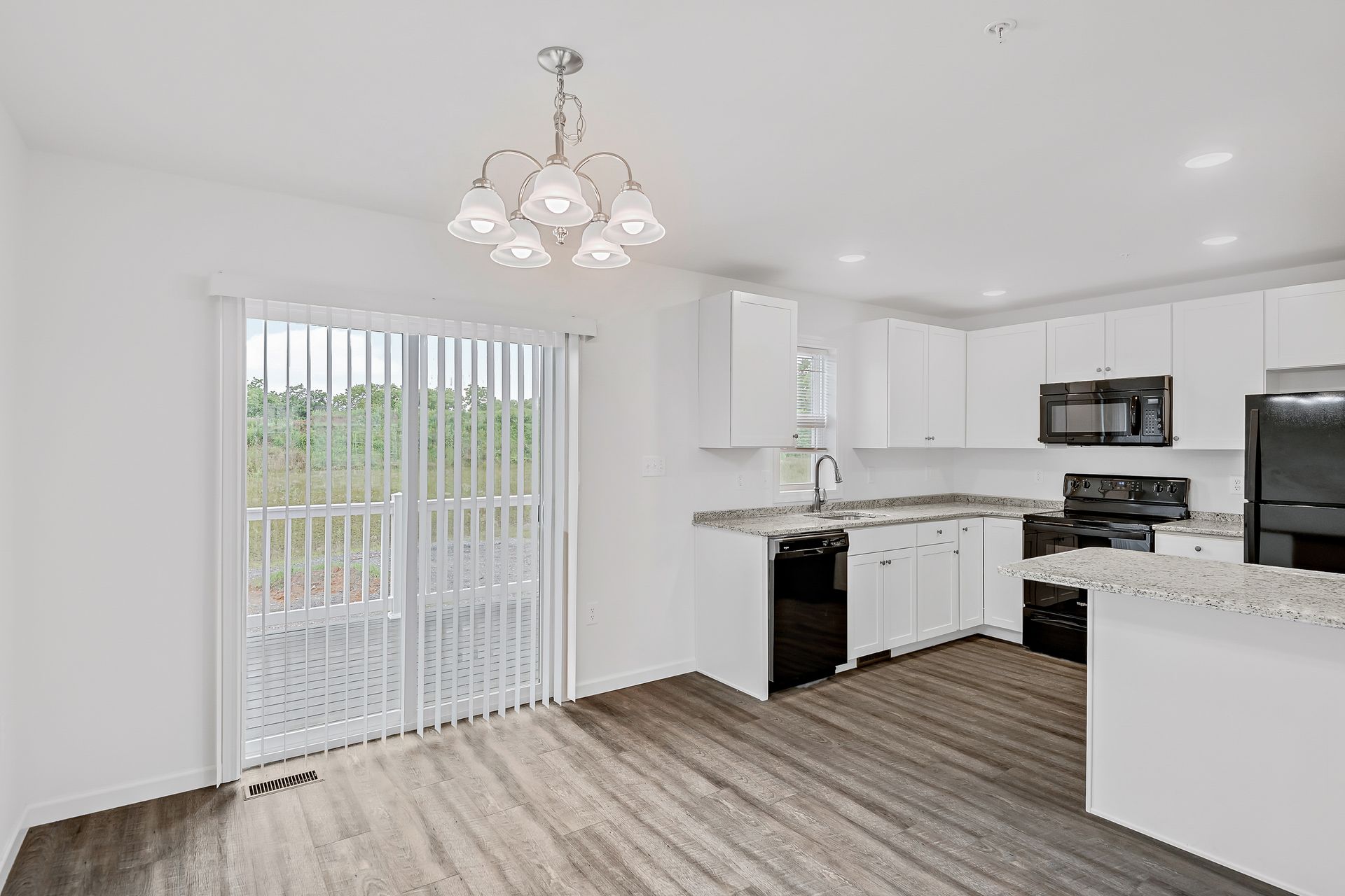 A kitchen with white cabinets and black appliances and a sliding glass door.