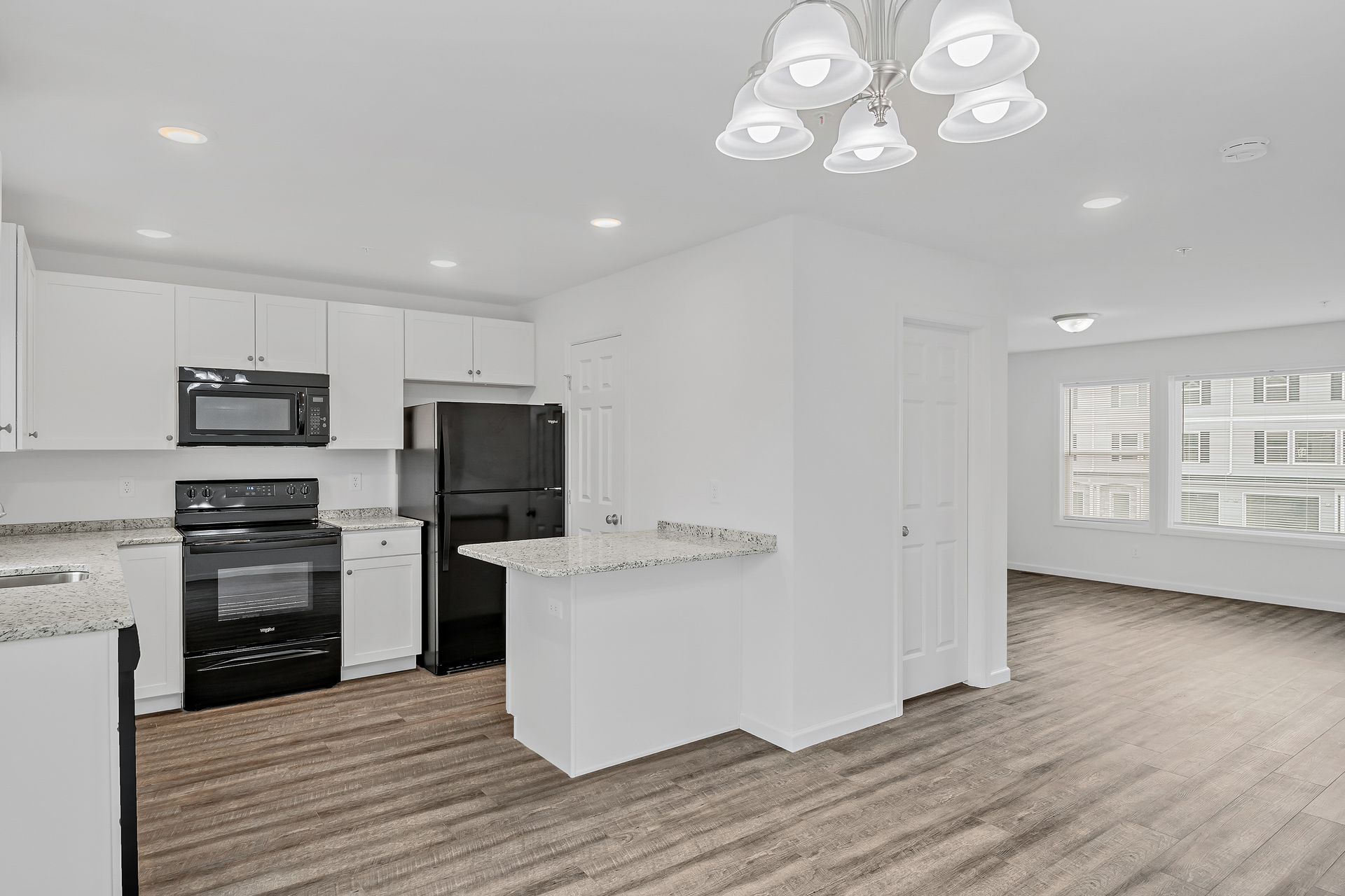 A kitchen with white cabinets , a black refrigerator , a microwave , and a wooden floor.