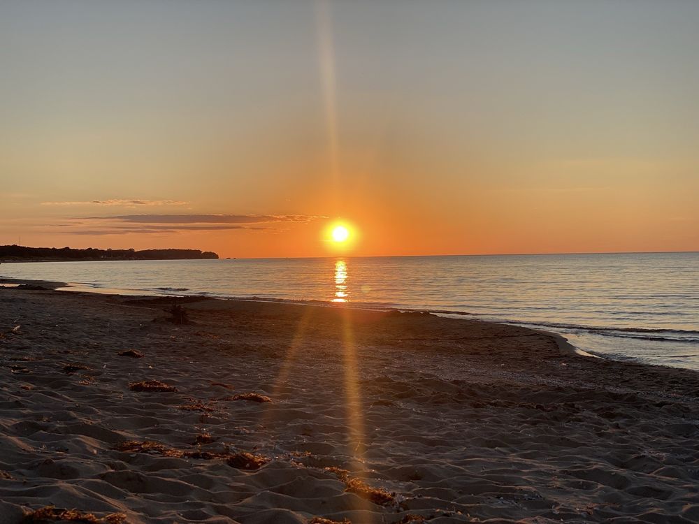 Sunset over a calm sea, with the sun's reflection on the water. Beach in foreground.
