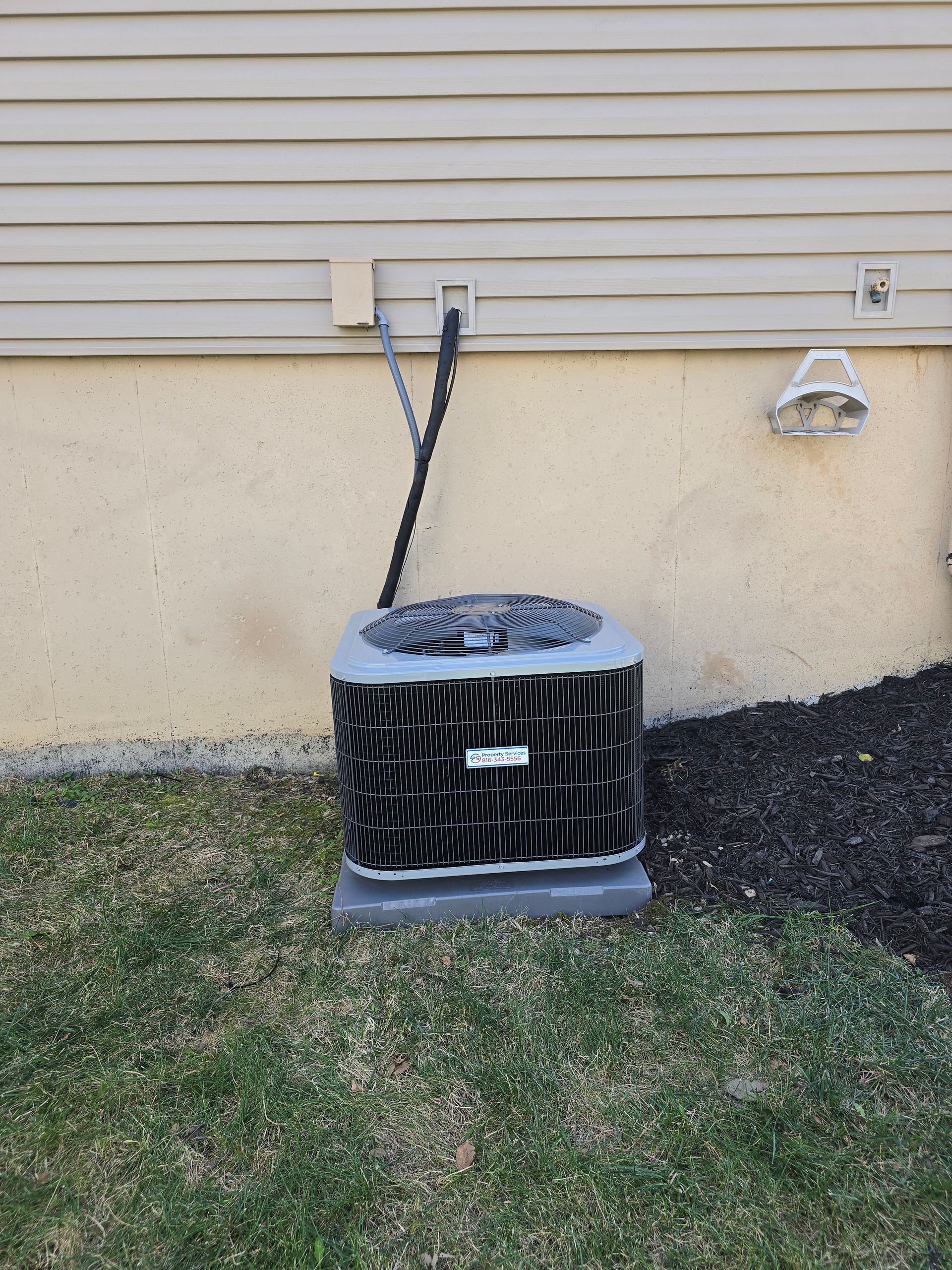 An outdoor air conditioning unit sits on a concrete pad against a house with light beige siding and a stucco foundation.