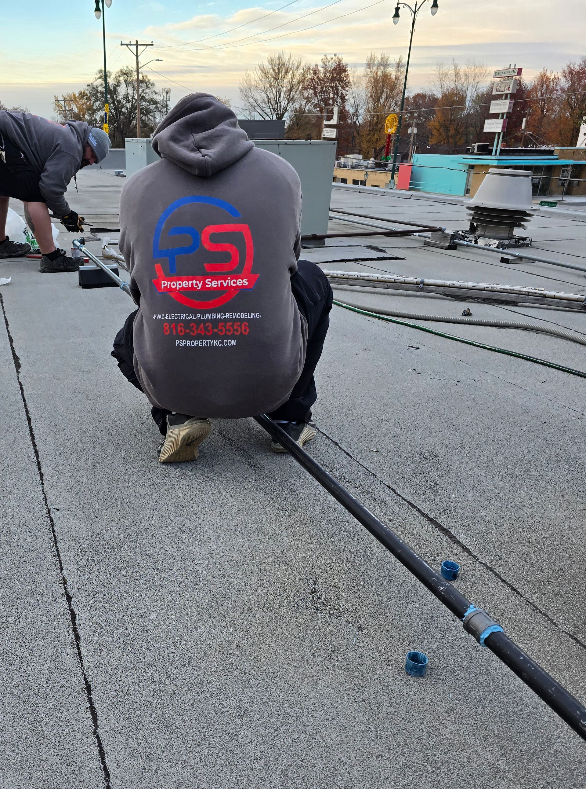 Two workers in grey hoodies install a cable on a flat, gravel-covered roof during the daytime.