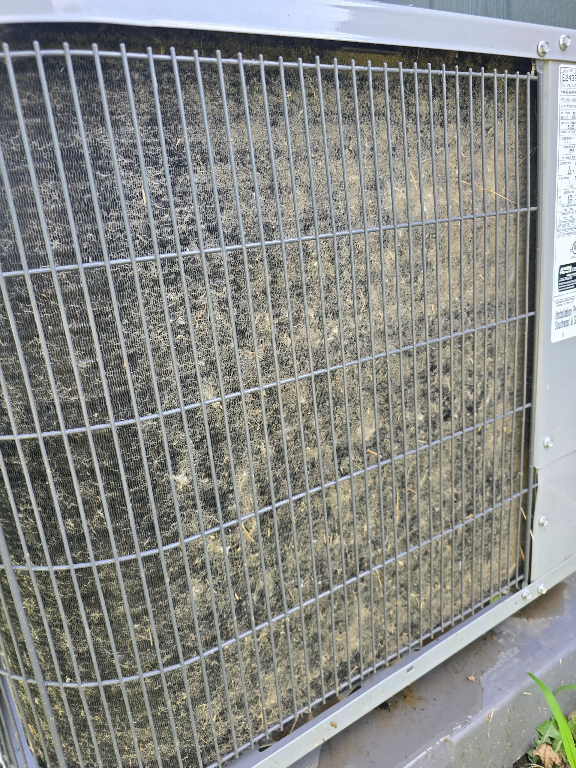 A close-up view of an outdoor air conditioning unit coil heavily clogged with dust, dirt, and debris.