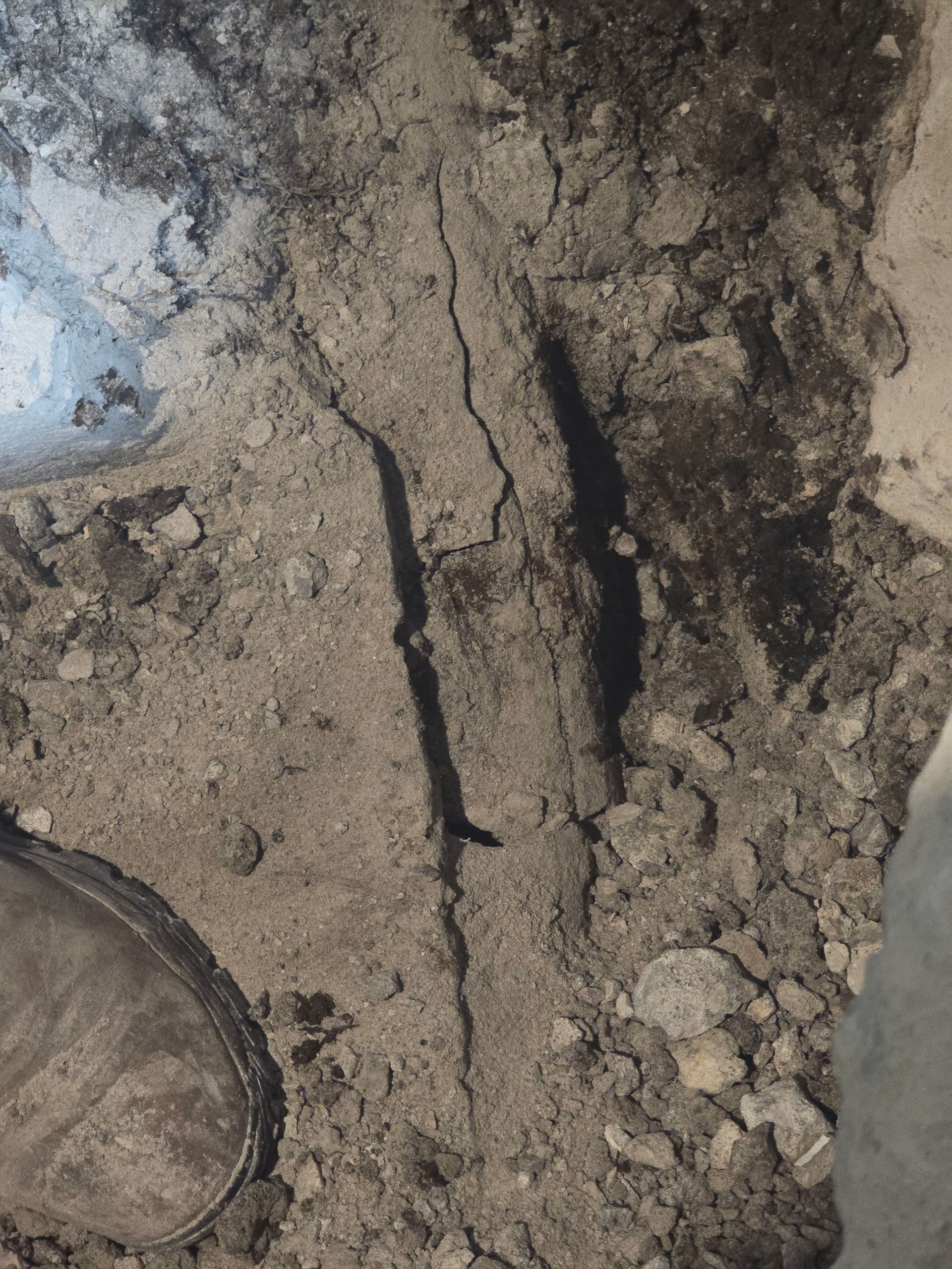 A crack runs through light-colored, loose soil or sand next to a work boot.