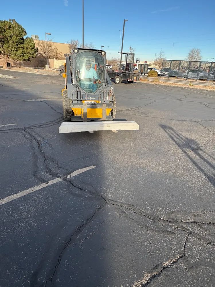 Small construction vehicle with front blade on cracked asphalt lot in daylight