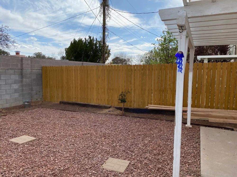 Backyard with gravel ground, wooden fence, concrete patio, and white post under a cloudy sky