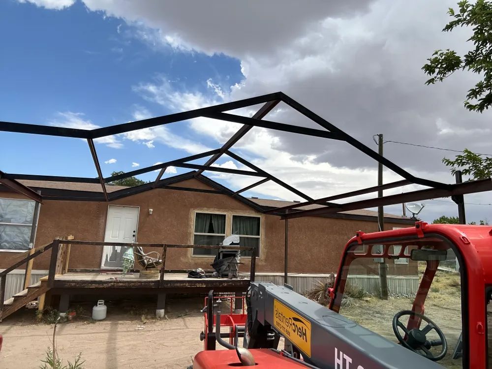 Partially built roof frame over a brick house, with a red lift in the foreground and cloudy sky above