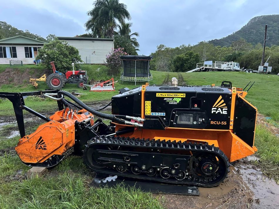 A Small Orange and Black Machine is Parked in a Grassy Field — NQ Steep Terrain Mulching and Clearing in The Leap, QLD