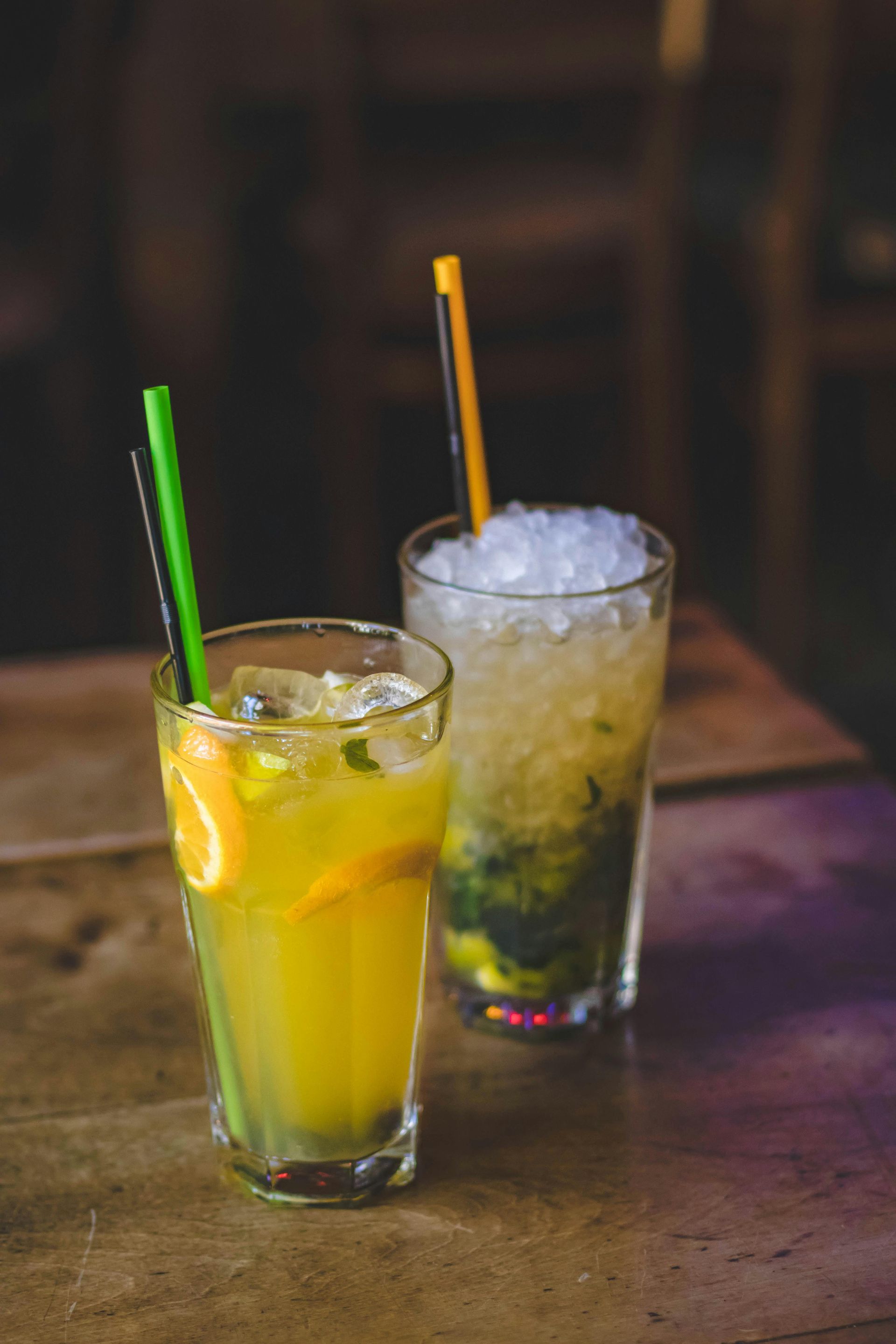Two drinks with straws on a wooden table.