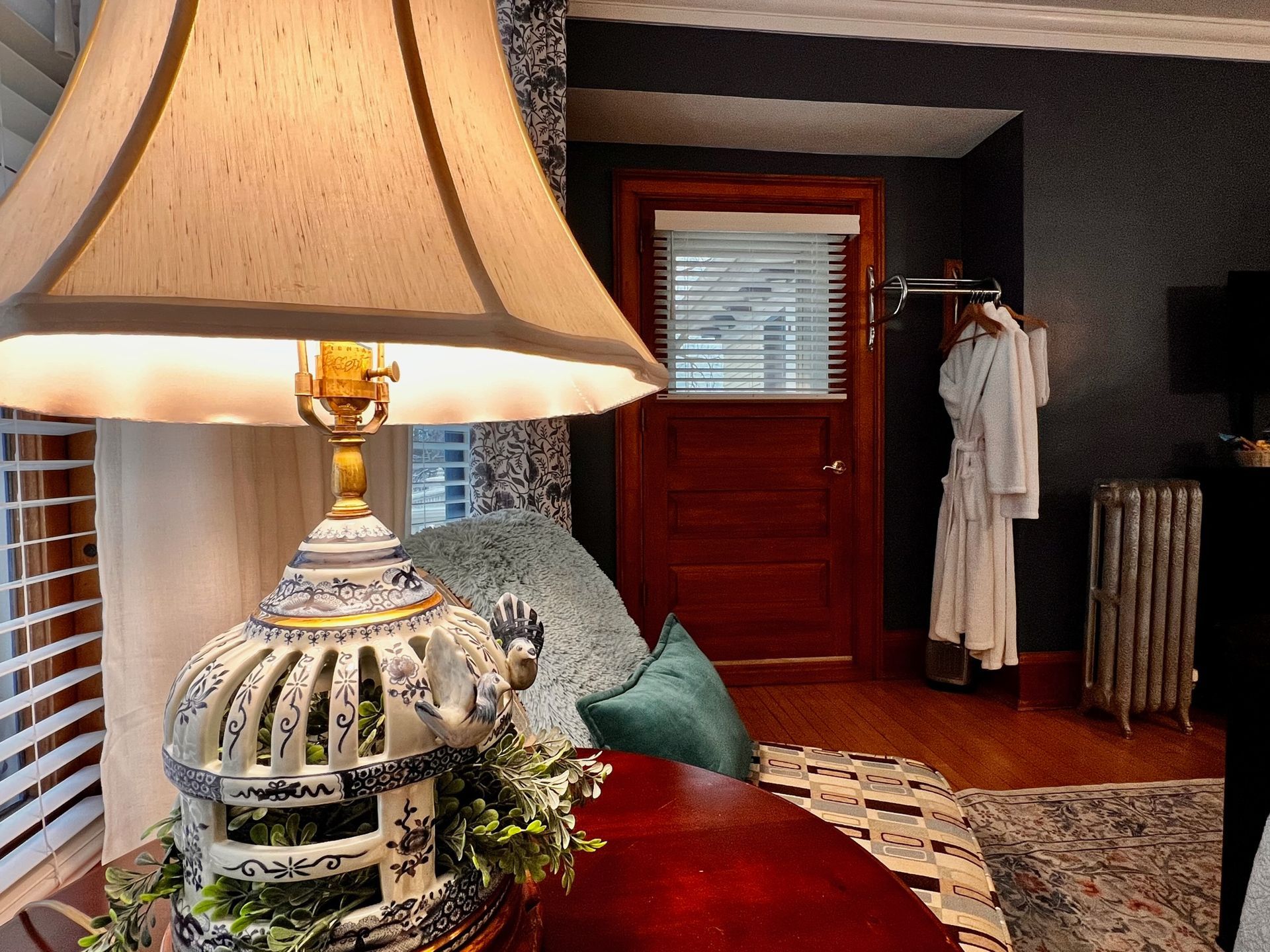 A cozy bedroom interior featuring a lit lamp on a table, a door with a robe hanging behind it, and a seating area.