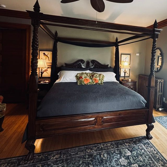 Four-poster dark wood bed with black bedding and floral pillow in a warmly lit bedroom