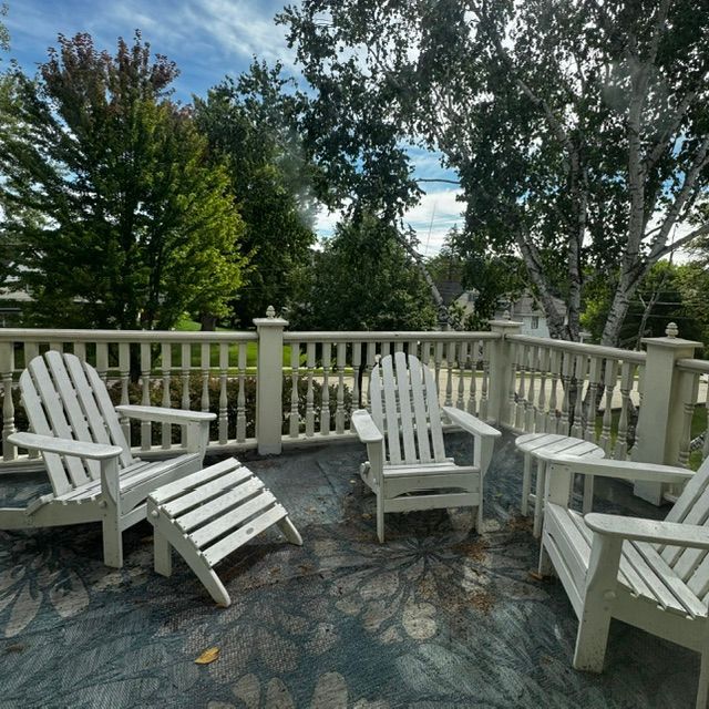 White Adirondack chairs on a stone patio overlooking a tree-filled garden and railing.