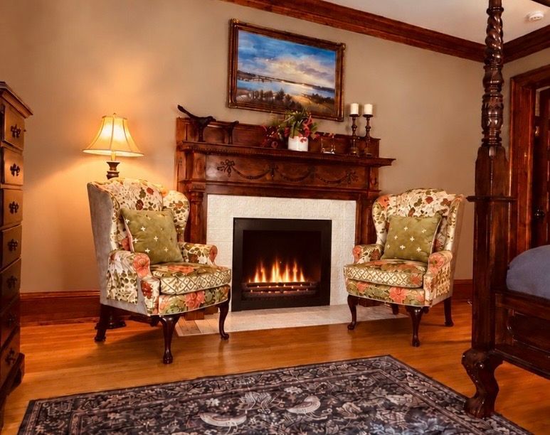 Two floral armchairs beside a lit fireplace with original white tiles at Honeybee Inn in Horicon, Wisconsin