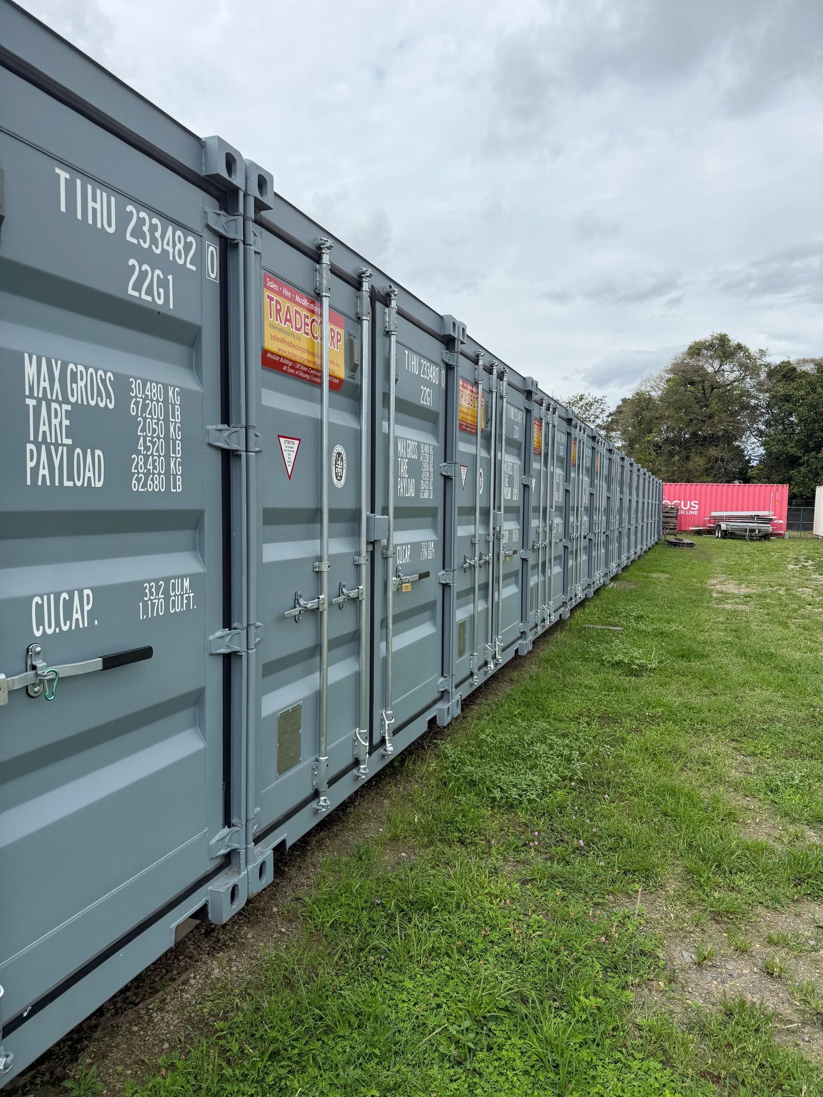 A row of gray shipping containers in a grassy area on a cloudy day.— Cairns Budget Storage In Mount Sheridan, QLD