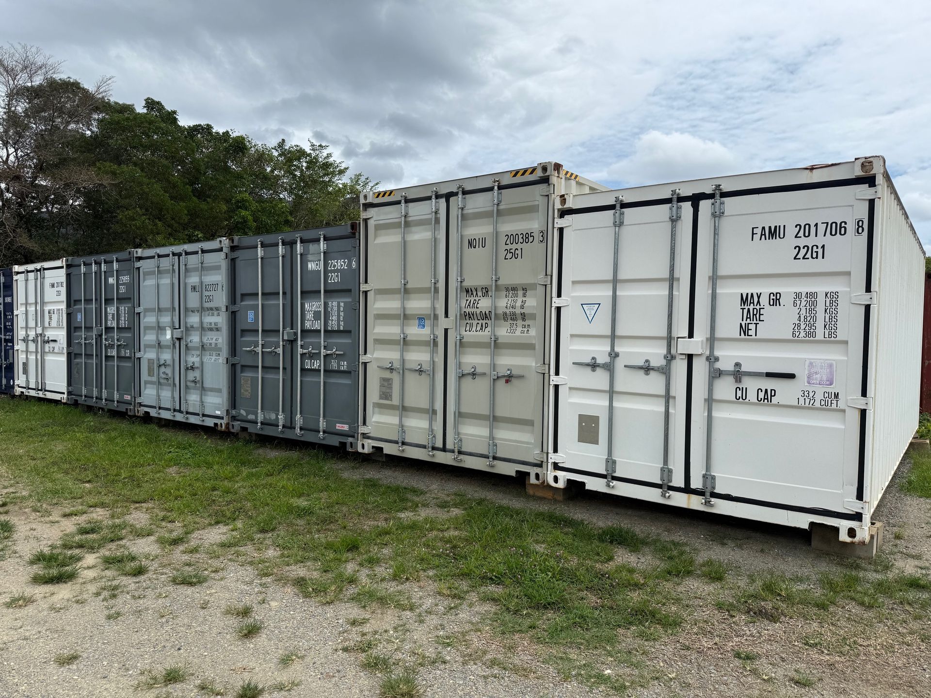 Shipping containers of various colors lined up on grassy ground.— Cairns Budget Storage In Mount Sheridan, QLD