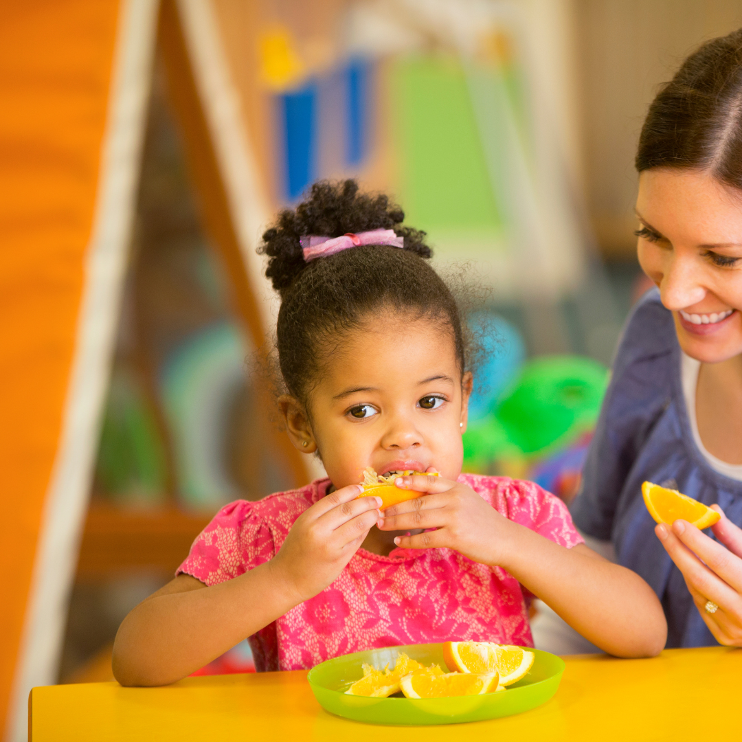 A woman and a little girl are sitting at a table eating oranges.