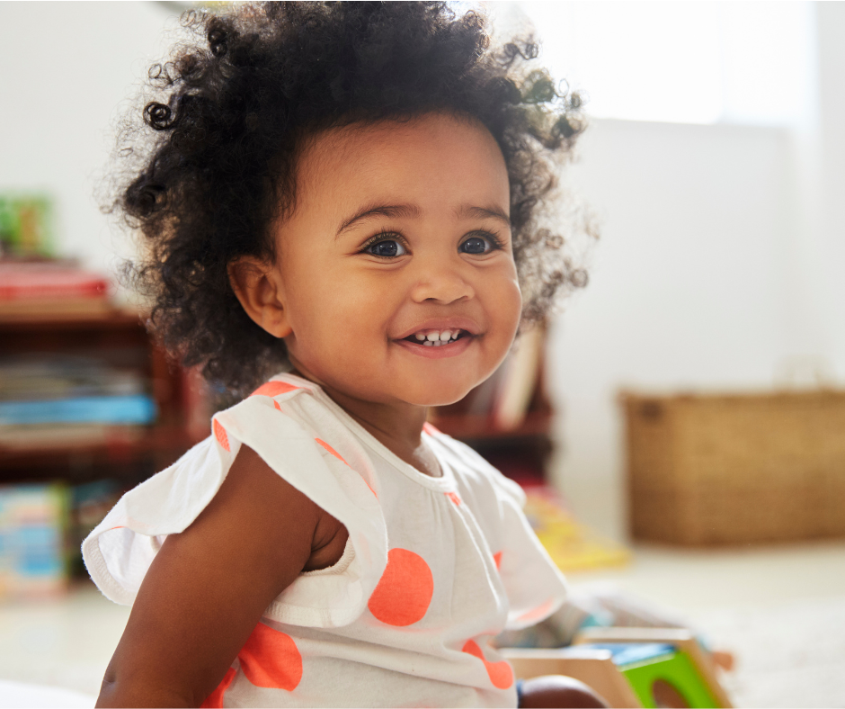 A little girl is sitting on the floor smiling at the camera.
