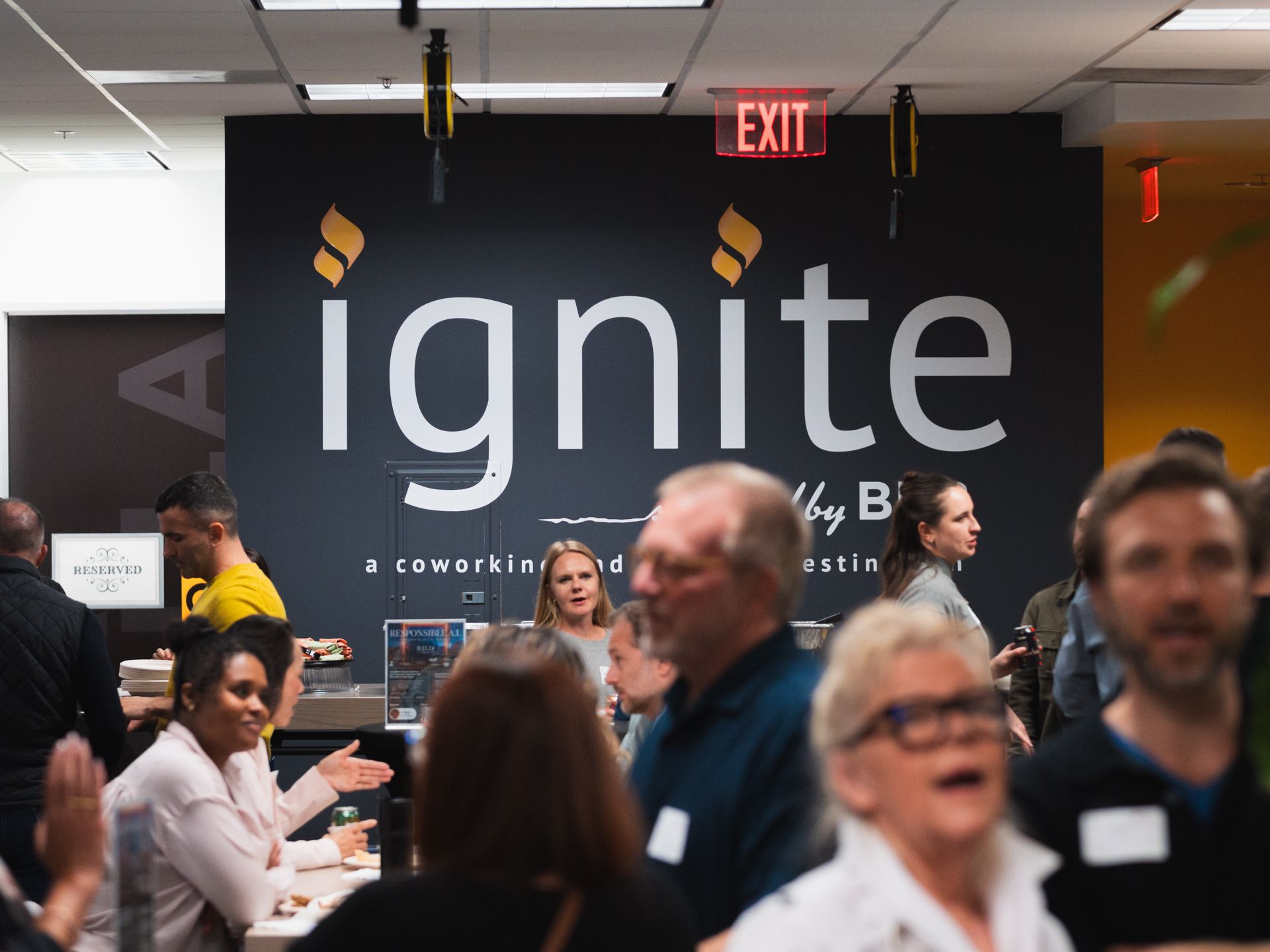 Crowded networking event with a large “ignite” sign on a black wall and people talking at tables