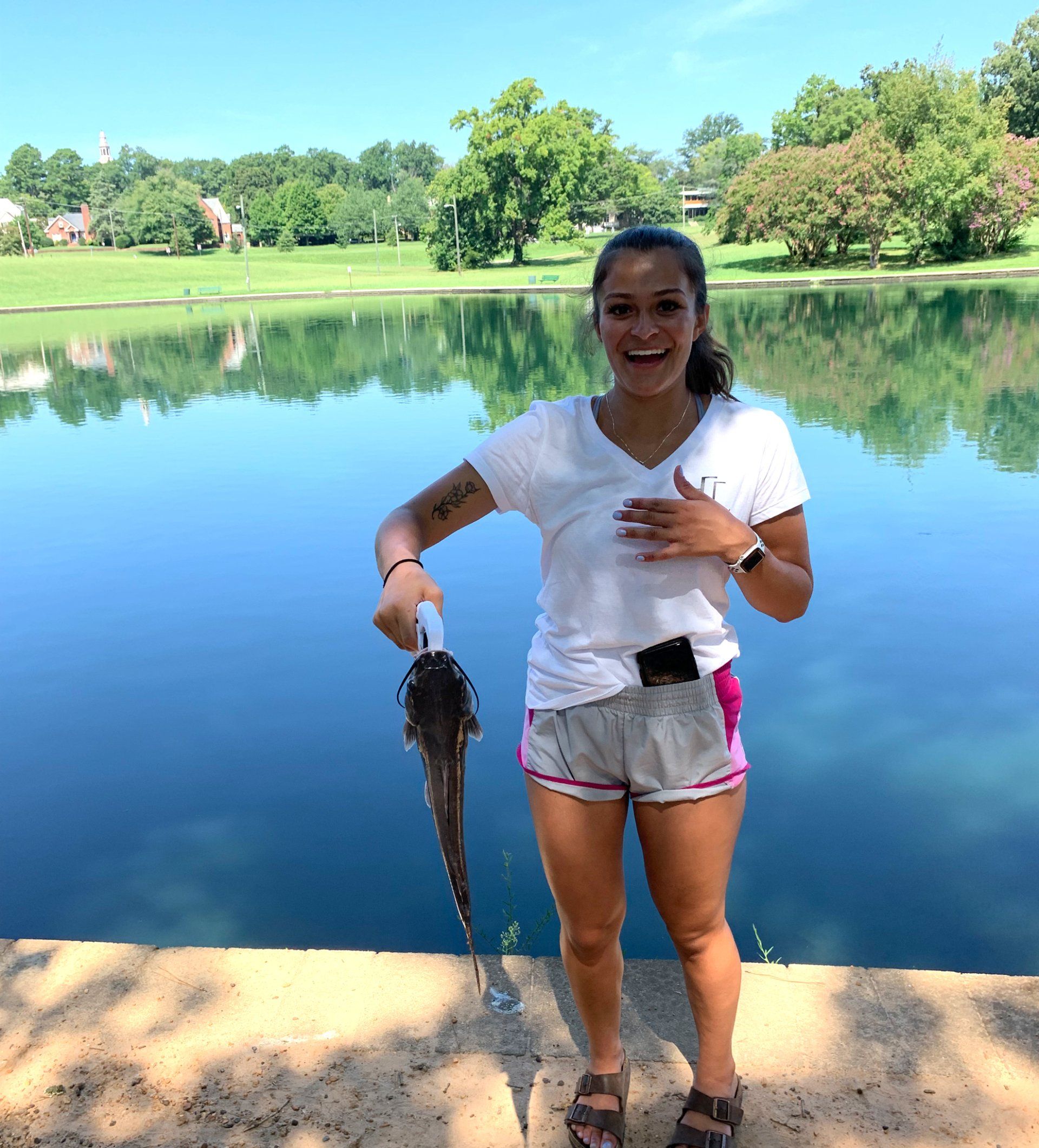 A woman is holding a fish in front of a lake.