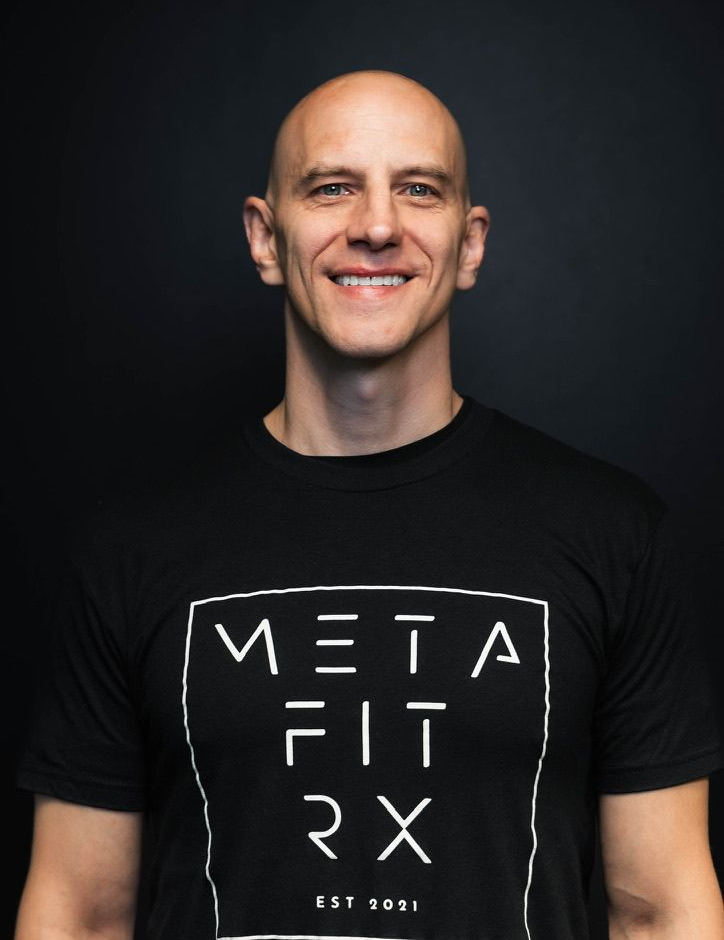 Smiling bald man in a black MetaFit RX T-shirt against a dark background