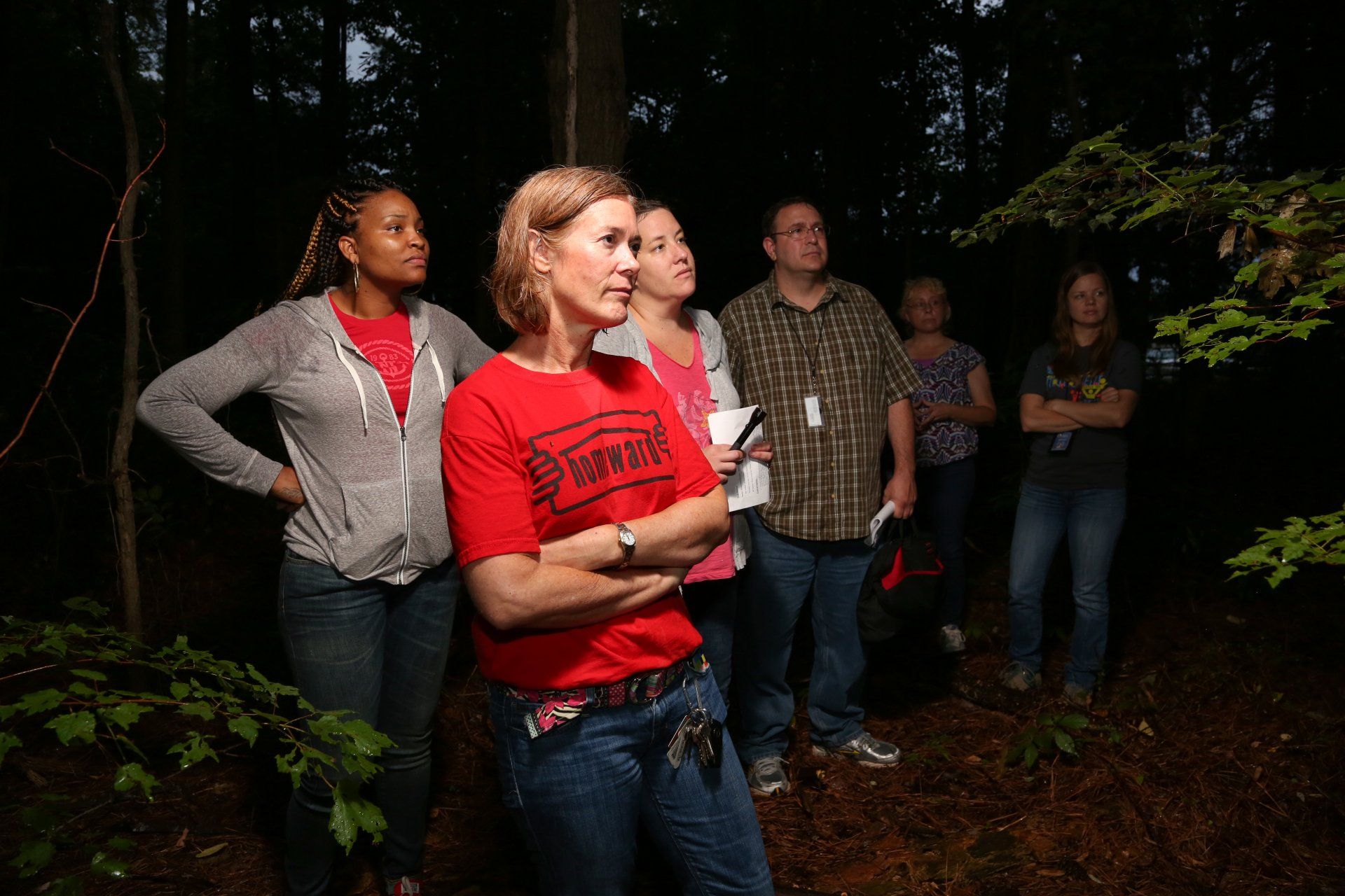 A group of people are standing in the woods looking at trees.
