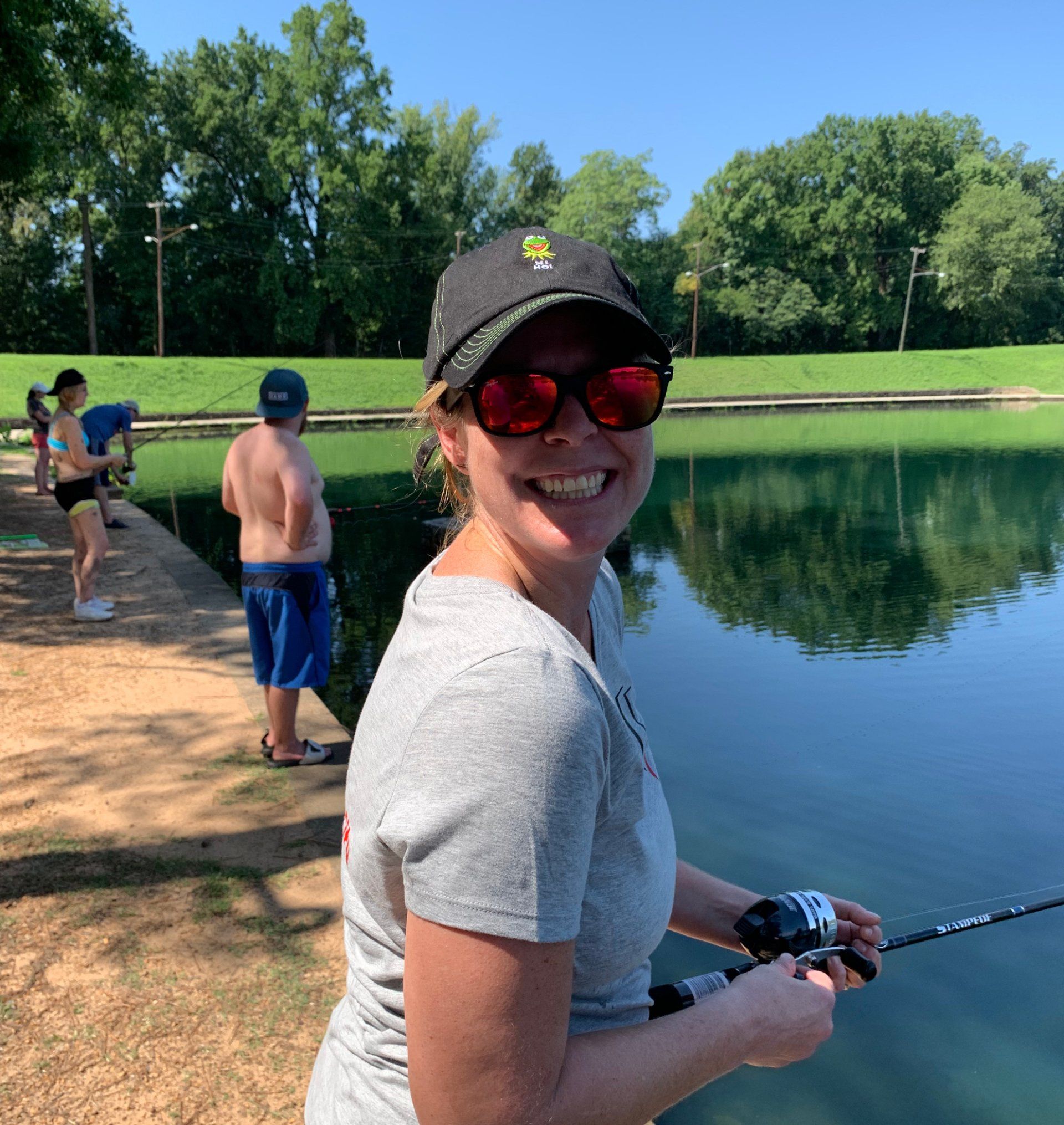 A woman wearing sunglasses and a hat is fishing in a lake.
