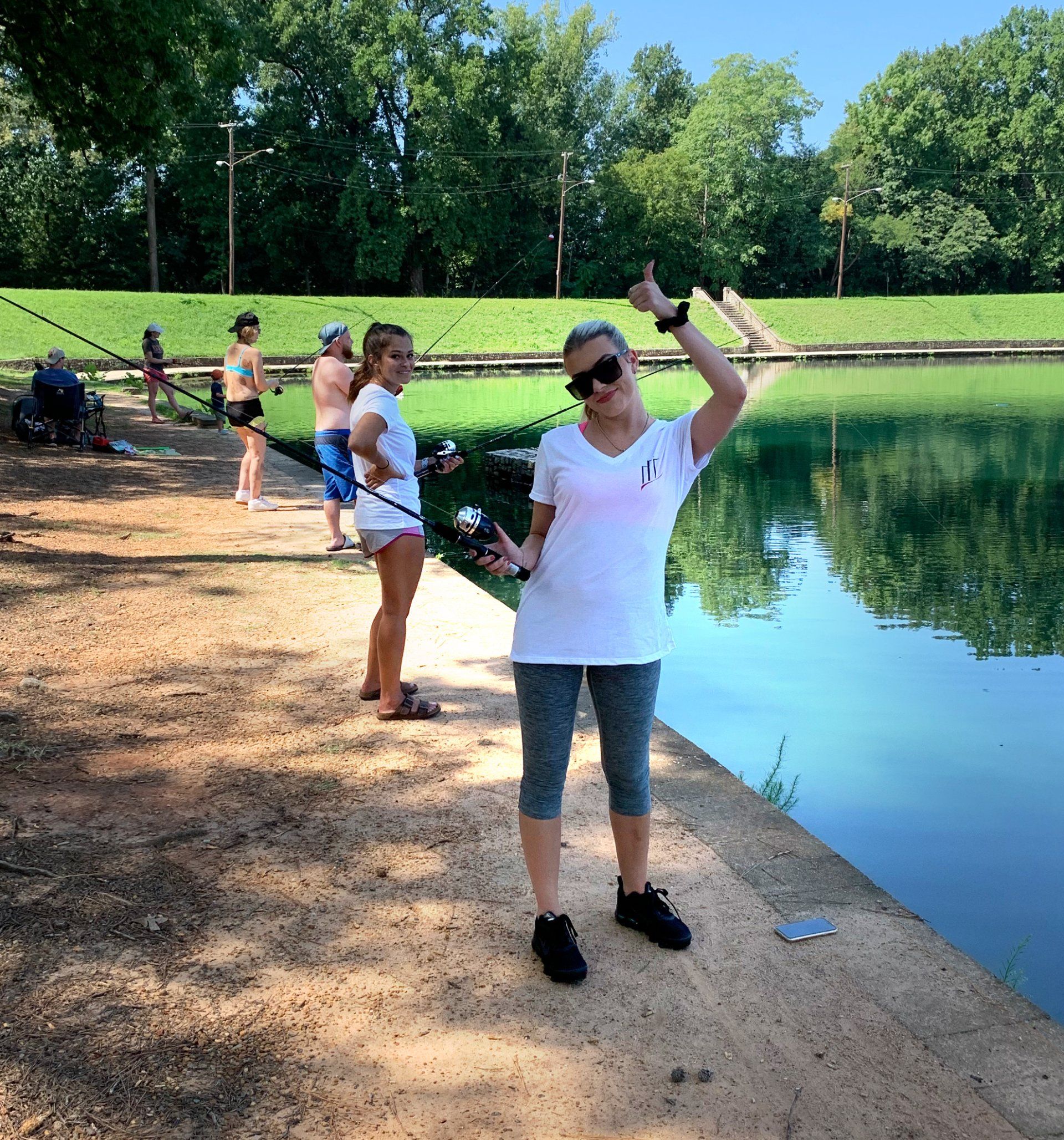 A woman is standing on the shore of a lake holding a fishing rod.