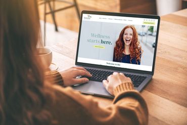 Woman using laptop with wellness website on screen.