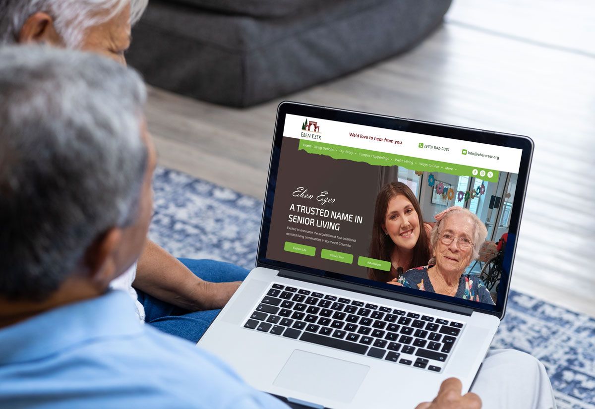 An individual uses a laptop to view a webpage for an elderly care service, featuring photos of caregivers and seniors.