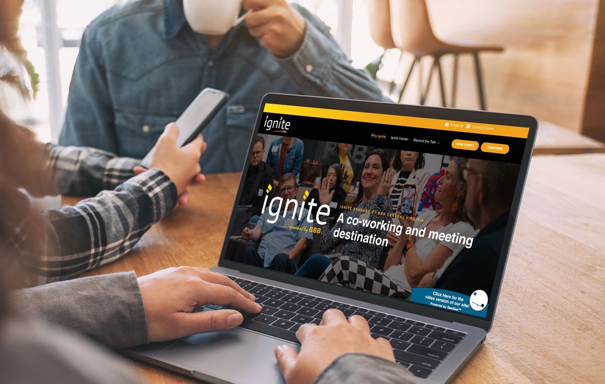 People using a laptop on a wooden table, displaying the Ignite website featuring a banner of a group gathering.