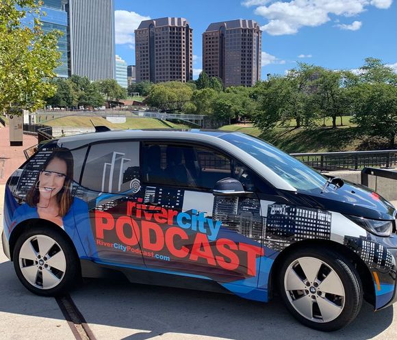 A river city podcast car is parked in front of richmond va skyline