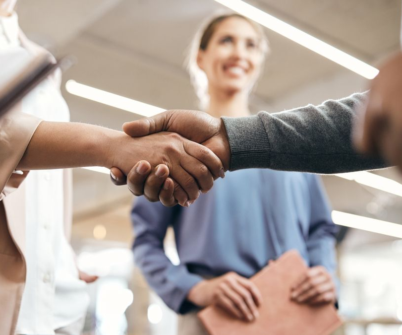 Two people shaking hands in an office, with a smiling colleague standing behind them.