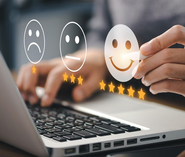 Hand placing smiling rating icon above laptop keyboard, with faded sad and neutral icons nearby