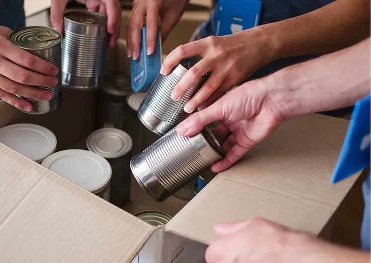 Hands packing canned goods into a cardboard box for donation.