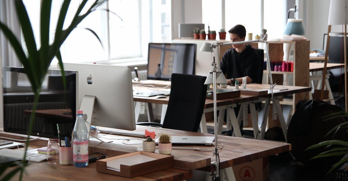 Person sitting at a desk in an office with a computer, surrounded by supplies.