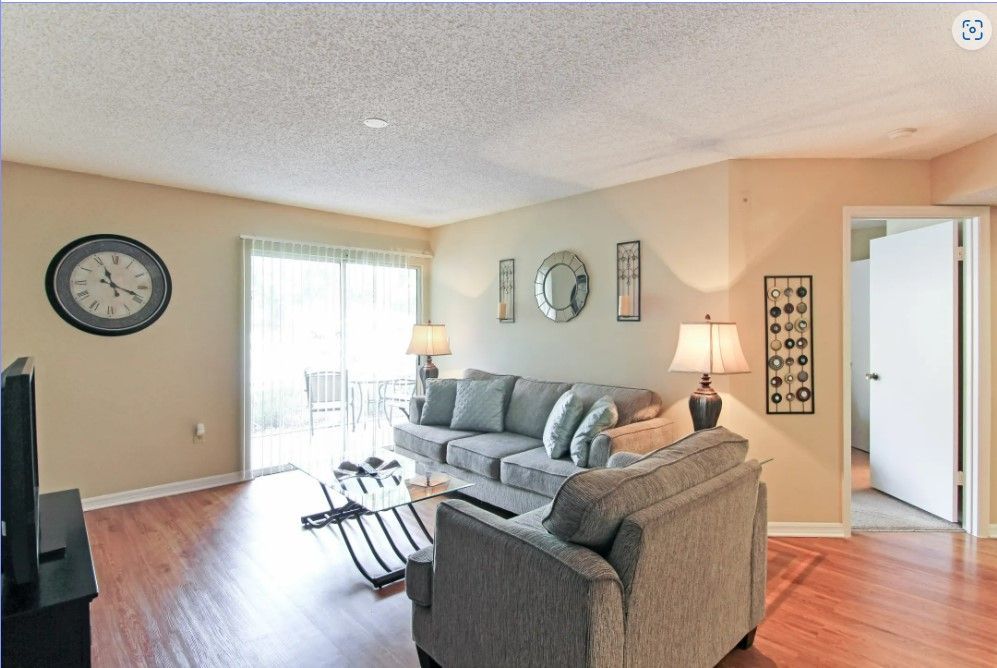Living room with gray sofa, clock, sliding glass door, and wooden floor.