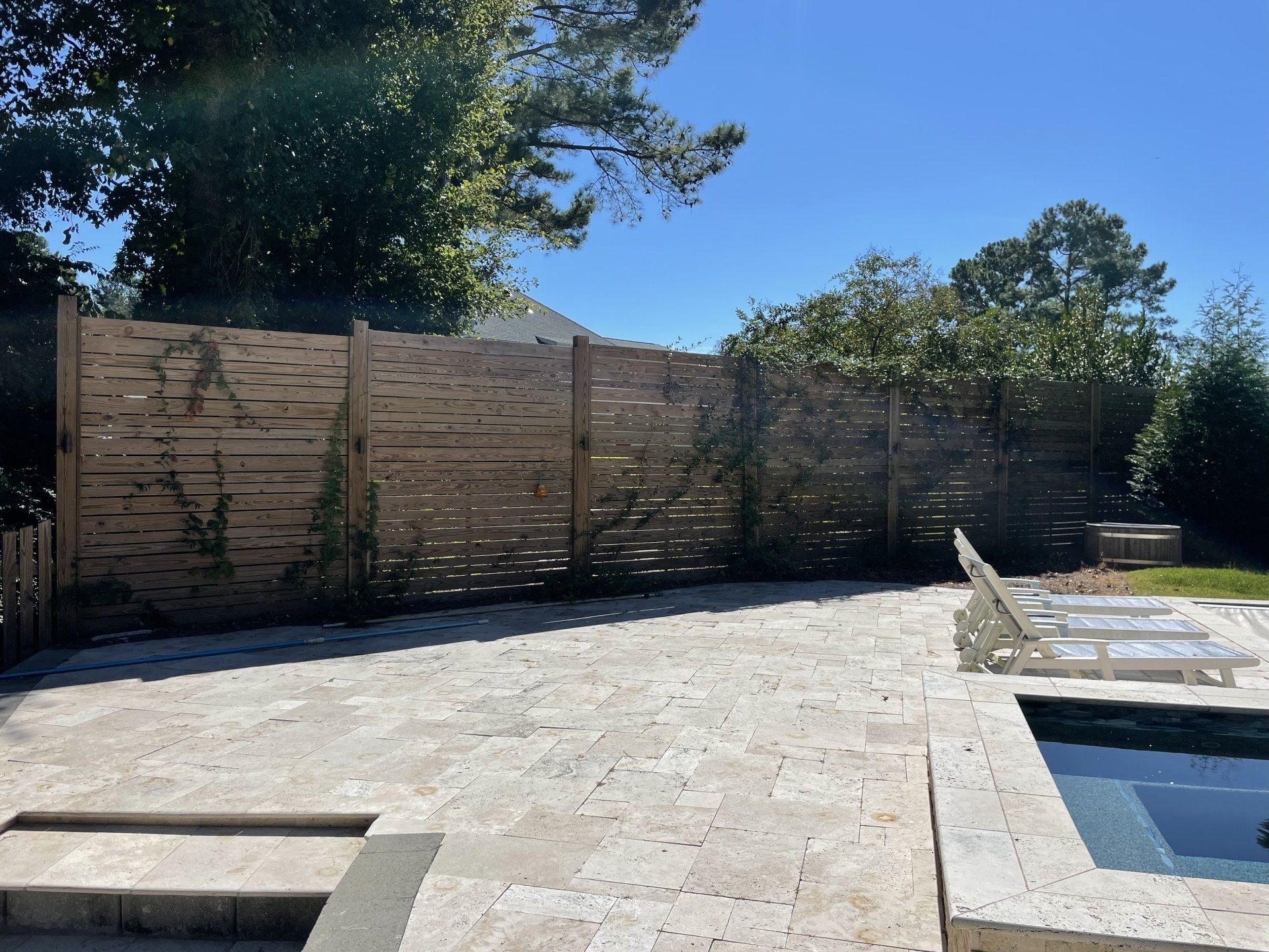 A wooden fence surrounds a patio with a pool in the background.