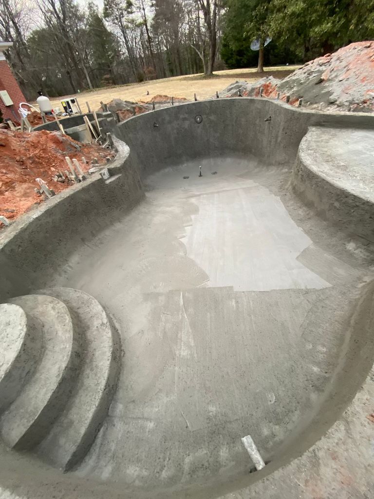 A large concrete pool is being built in a backyard.